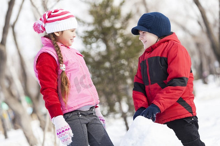 小游戏冲鸭摄影照片_可爱的男孩和女孩在冬季公园堆雪人。冬季活动小游戏