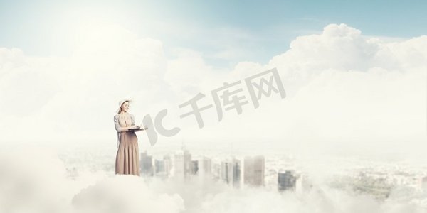 云层上摄影照片_带着笔记本电脑的复古女孩。站在云端使用笔记本电脑的年轻女士