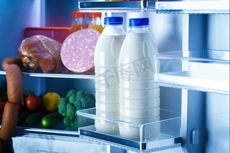冰箱里的水果摄影照片_敞开的冰箱里装满了食物。关注冰箱里的几瓶牛奶