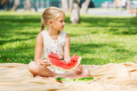 吃西瓜的女孩。公园里的可爱女孩吃着多汁的西瓜