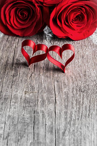 两朵玫瑰和丝带心在木背景，情人节