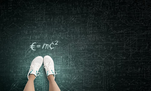物理学中的公式。穿运动鞋的女孩站在黑板上的俯瞰