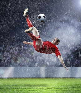 足球运动员击球。在红色衬衫的足球运动员在雨中在体育场击球