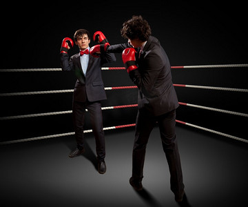 男人打拳摄影照片_两个年轻的商人在打拳击。两个年轻的商人在黑暗的背景下打拳。概念拼贴