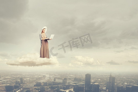带着笔记本电脑的复古女孩。站在云端使用笔记本电脑的年轻女士