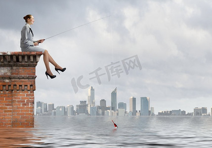 钓鱼概念女商人钓鱼与杆在建筑物顶部