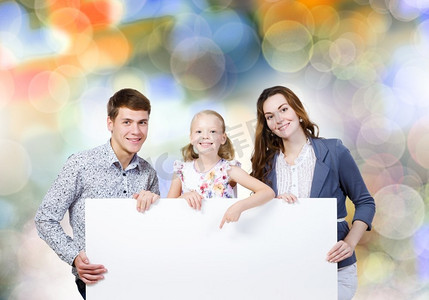 快乐家庭海报摄影照片_年轻的家庭。幸福的一家三口举着白色的空白横幅。文本位置