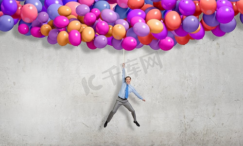 一位年轻的成功商人骑着一堆五颜六色的气球飞行。天空中飞翔的人