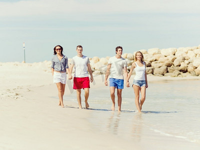 海洋公司摄影照片_海滩上的年轻人。公司的年轻朋友在海滩上沿着海岸散步
