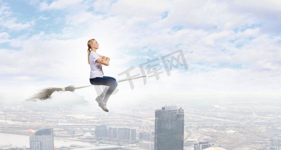 穿着休闲的少女骑着扫帚在高空飞翔。扫帚上的女孩