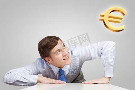 年轻人从桌子下面看着欧元符号。如何赚钱？