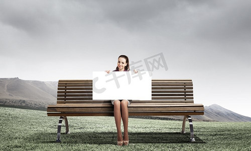 魏国献礼摄影照片_献礼的女孩。坐在板凳上的年轻女子举着白色的横幅