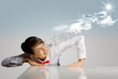 漂亮空姐摄影照片_空姐。一名年轻女子俯身在桌子上方，看着天空中的飞机
