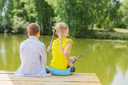 夏日休闲。后视图的两个孩子坐在银行和钓鱼