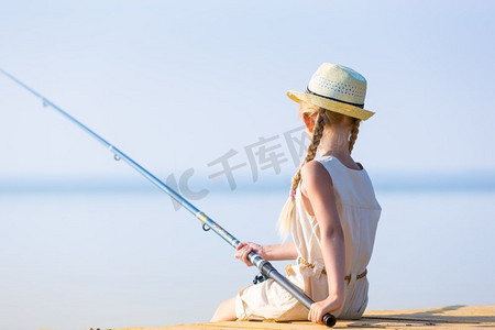 连衣裙帽子摄影照片_穿着连衣裙戴着帽子的女孩在码头钓鱼
