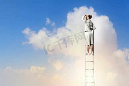 站在梯子上的女商人。站在梯子上的女商人在多云的背景下眺望远方
