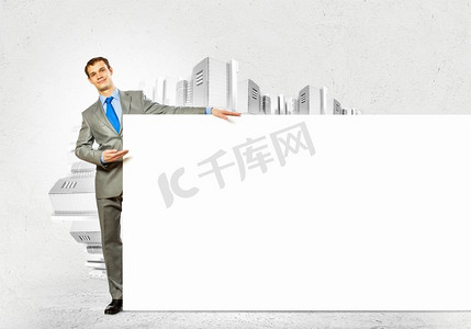 对立面摄影照片_打着空白横幅的商人。拿着空白横幅的商人站在城市风景的对立面。文本的位置