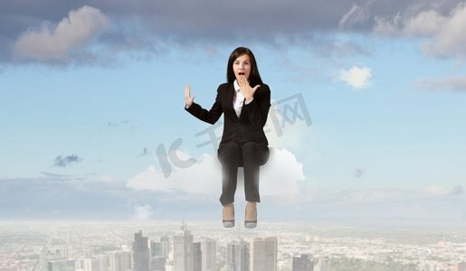 大吃一惊的女商人。年轻情绪化的女商人坐在城市上空的云端