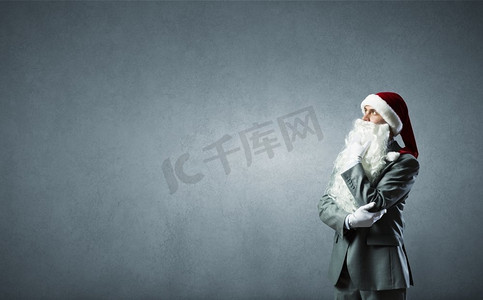 圣诞老人帽子摄影照片_商业圣诞老人。戴着圣诞老人帽子，手托着下巴的体贴的商人