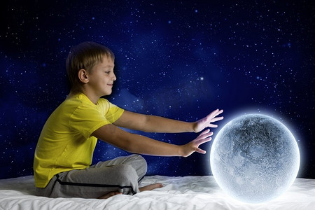 晚上做梦。可爱的男孩坐在床上与月球行星
