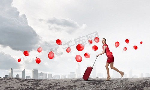 行李箱红色摄影照片_穿红衣服的女人。年轻女子在红色礼服与红色行李