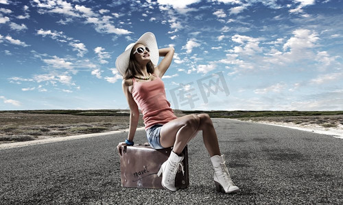 自动停止旅行。年轻漂亮的女孩坐在路边的行李箱里