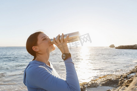 一名妇女在海滩上喝水。年轻女子在海滩上运动后喝水