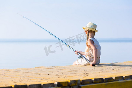 穿着连衣裙戴着帽子的女孩在码头钓鱼