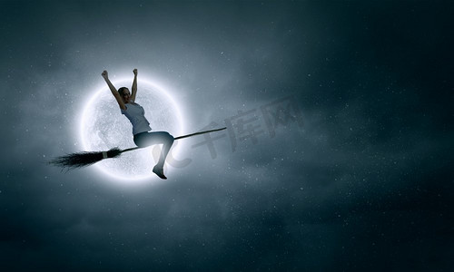 万圣节免费摄影照片_穿着休闲的少女骑着扫帚在高空飞翔。扫帚上的女孩