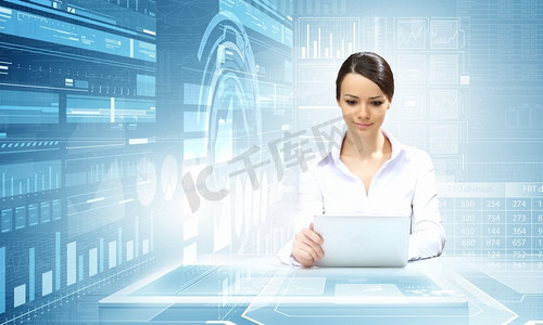使用现代科技的女性。坐在桌子旁的女商人手持平板电脑，背景是高科技的蓝色