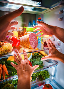 冰箱里的水果摄影照片_在敞开的冰箱里，人的手在晚上伸手拿食物