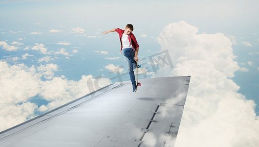 滑板男孩摄影照片_在飞机机翼上滑冰的家伙。十几岁的男孩在机翼边缘滑板