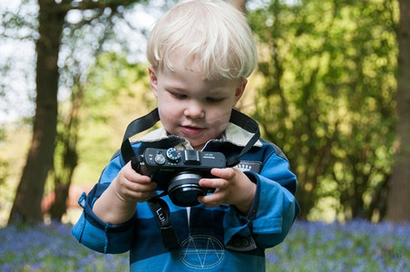 孩子拿着LUMIX相机，在一片蓝铃木中玩耍。