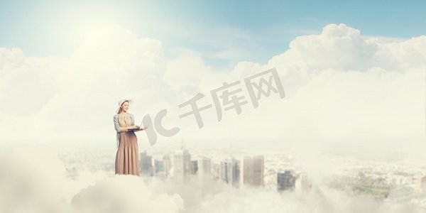 云层上摄影照片_带着笔记本电脑的复古女孩。站在云端使用笔记本电脑的年轻女士