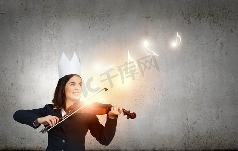 维奥拉摄影照片_表演女王年轻漂亮的女商人在纸皇冠演奏小提琴