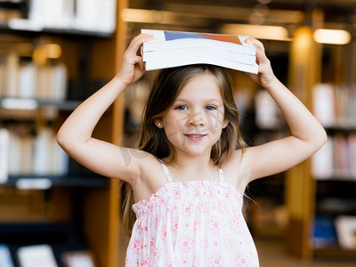 图书会摄影照片_图书馆里一个头顶着一本书的小女孩。阅读可能会很有趣