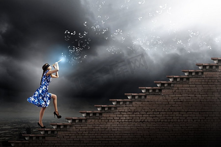 全新玩法摄影照片_吹长笛的女人。一位穿着蓝色连衣裙的年轻女子一边吹奏着笛子，一边爬着梯子
