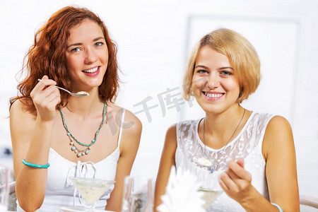 咖啡馆里的可爱女孩。两个年轻漂亮的女人坐在咖啡馆里吃着甜点