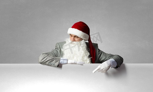 圣诞指向牌摄影照片_圣诞老人与横幅商人在圣诞老人帽子与白色空白横幅