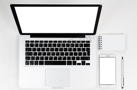 现代笔记本电脑，俯视。现代笔记本电脑和智能手机，白色桌子上有空白屏幕，可从上方观看
