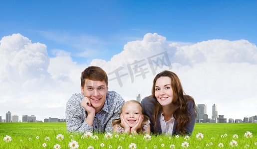 年轻的家庭。幸福的三口之家躺在绿草