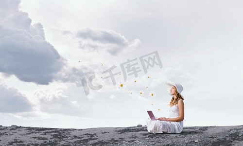 坐在山顶摄影照片_使用笔记本电脑的女士。坐在山顶上拿着笔记本电脑的年轻女士