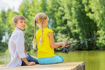 夏日休闲。后视图的两个孩子坐在银行和钓鱼