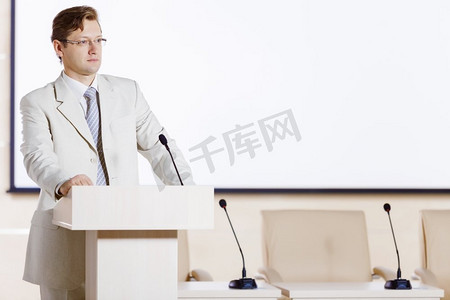 一位年轻的商人站在舞台上对着麦克风讲话。舞台上的演讲者