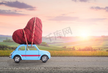 蓝色复古玩具车在模糊的托斯卡纳乡村日落风景的映衬下为情人节送去心意