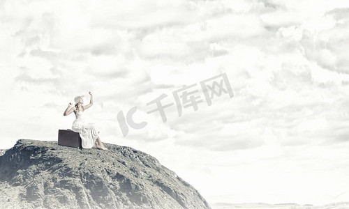 她轻装上阵。一位穿着白色长裙、戴着帽子的女子坐在山顶的行李上
