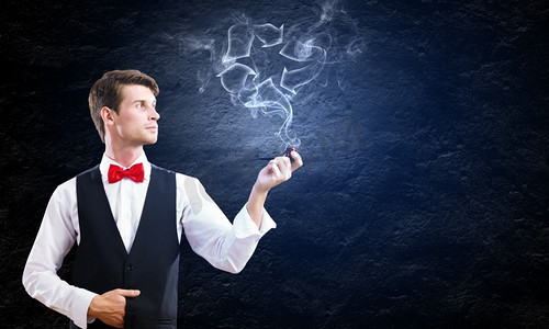 吸烟的人摄影照片_吸烟的烟斗。年轻英俊的商人在黑色背景下抽着烟斗