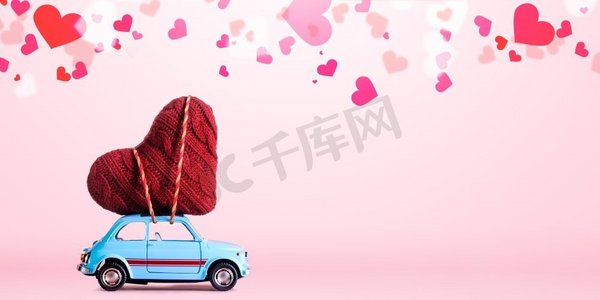 蓝色减速火箭玩具车交付情人节的工艺心脏在粉红色背景与五彩纸屑