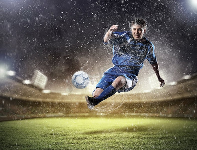 足球运动员击球。一个穿着蓝色球衣的足球运动员在雨中把球踢到了体育场的高处