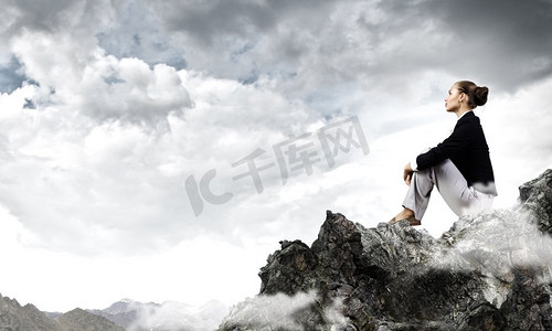坐在山顶摄影照片_在上面。年轻漂亮的女商人坐在山顶